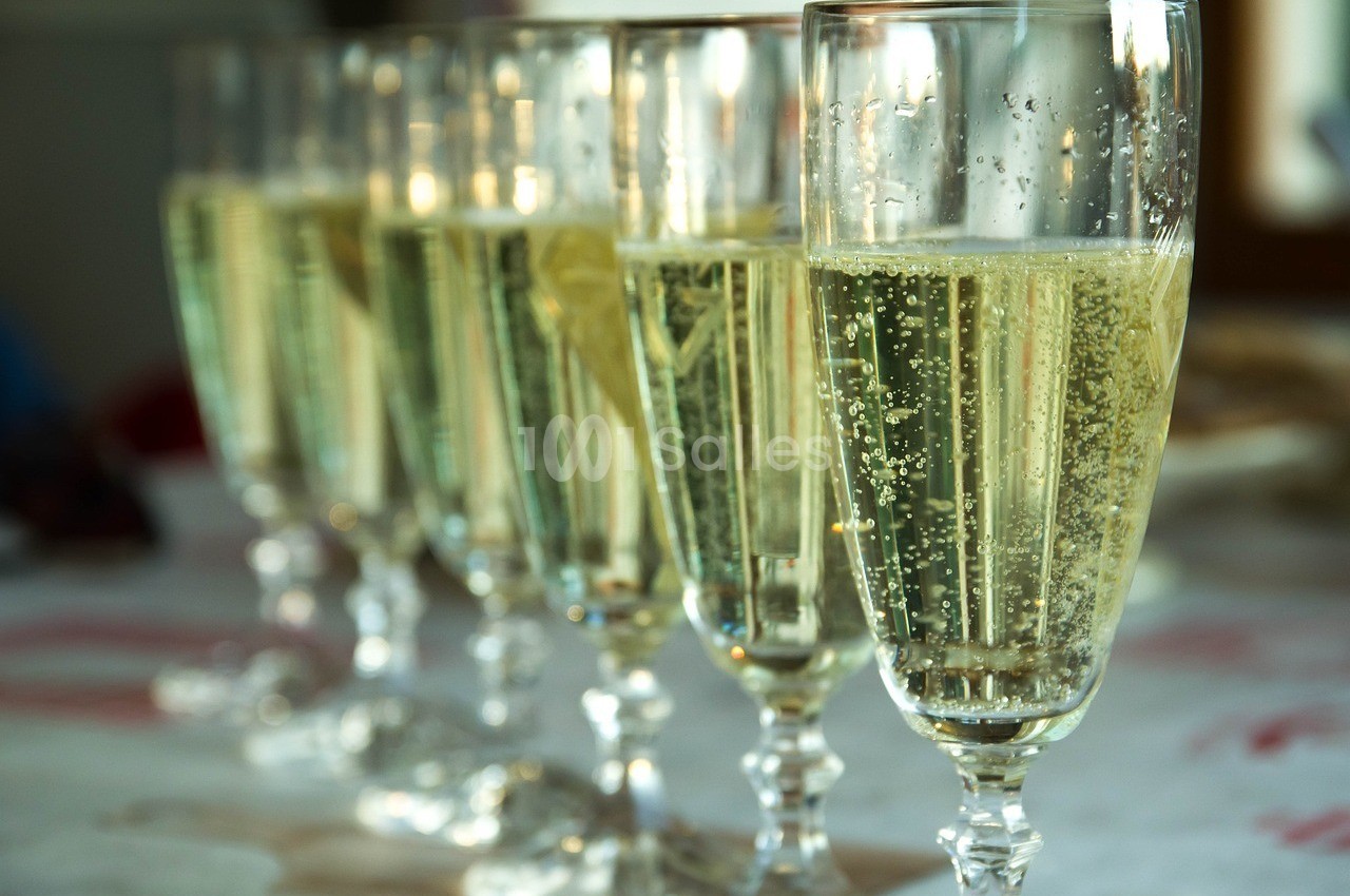 Six flûtes remplies de champagne alignées sur une table blanche.