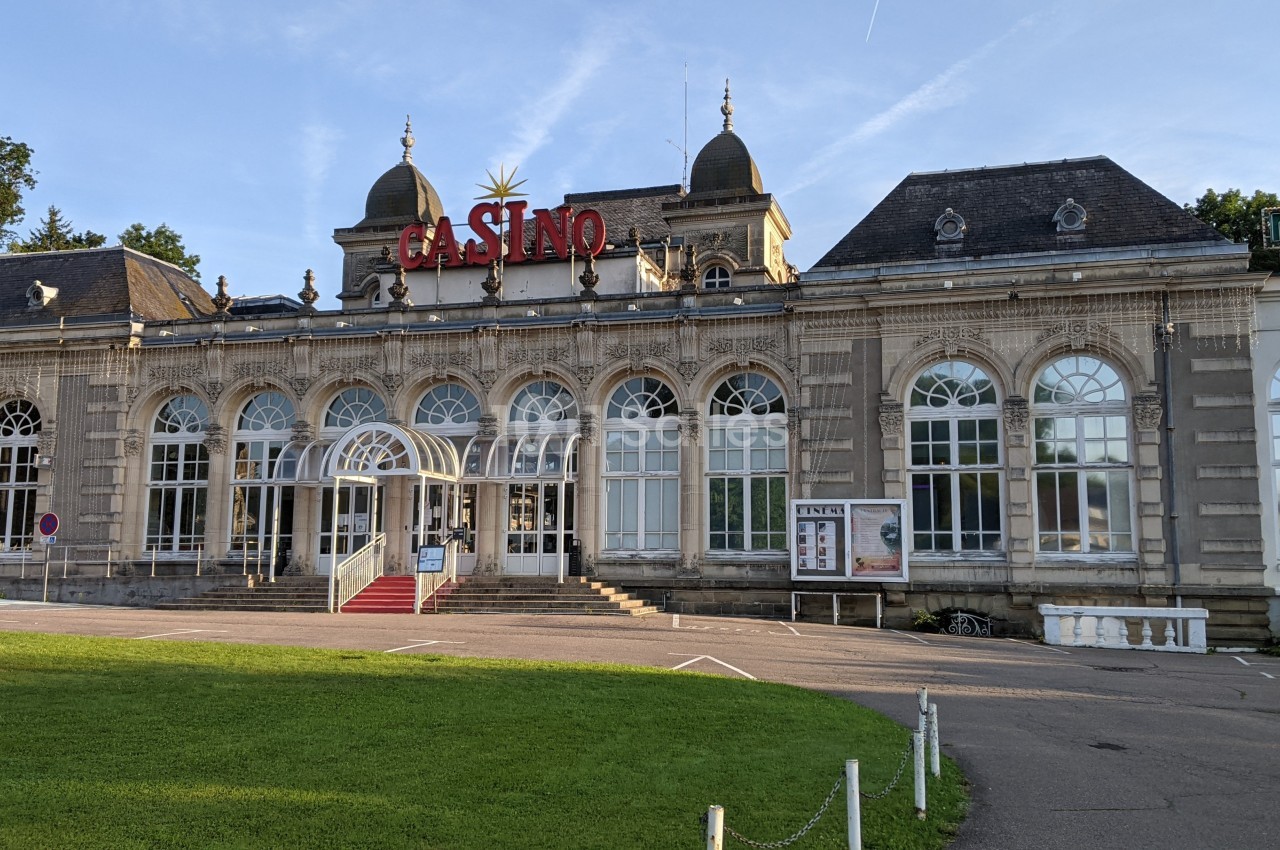 Façade d'un bâtiment ancien avec des arches vitrées, abritant un casino, entouré de pelouse et d'arbres.
