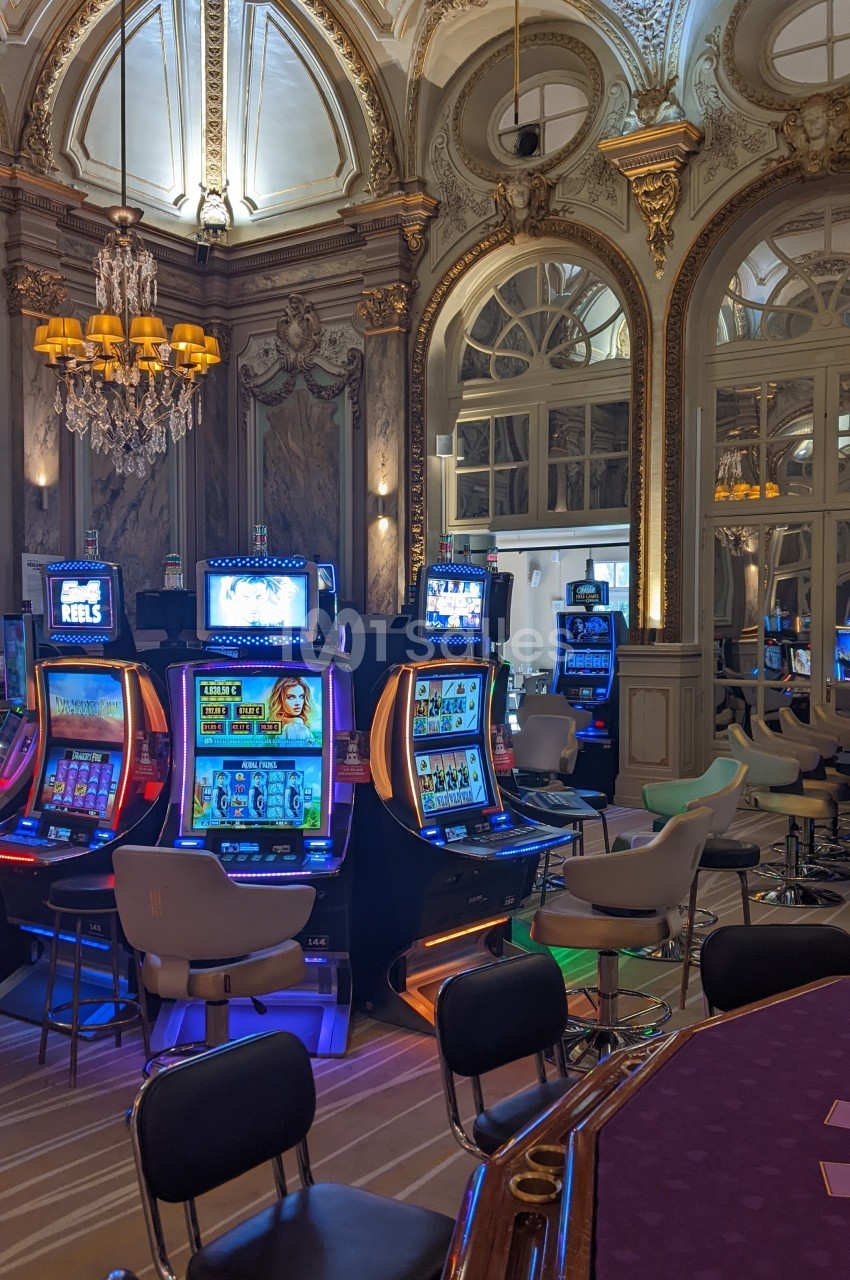 Salle de casino élégante avec machines à sous illuminées, décorations classiques et lustre imposant.