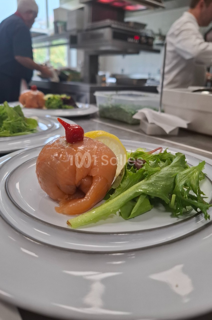 Assiette avec un roulé de saumon fumé garni d'un piment rouge, accompagné de salade verte et d'un quartier de citron.