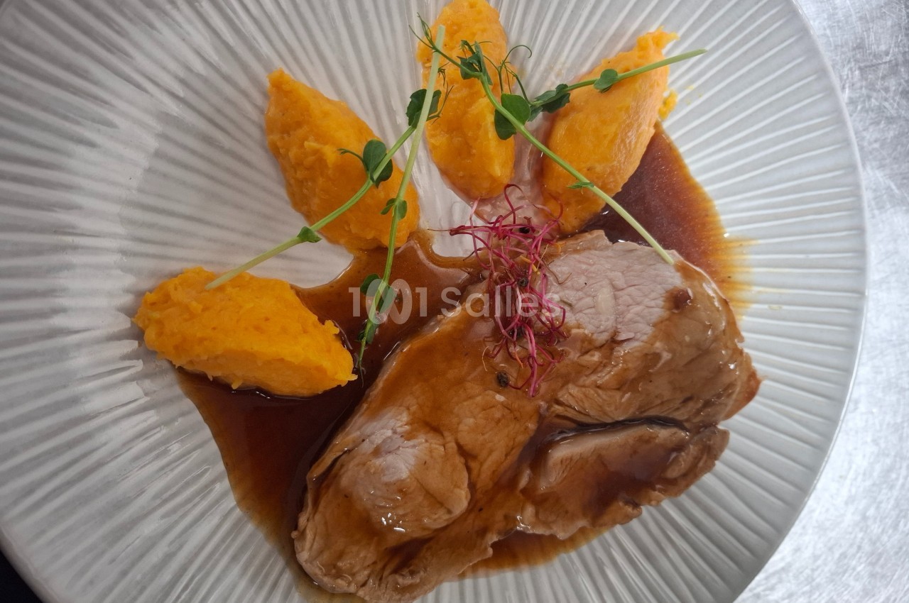 Assiette avec des tranches de viande nappées de sauce, accompagnées de purée de carottes et décorées de pousses.