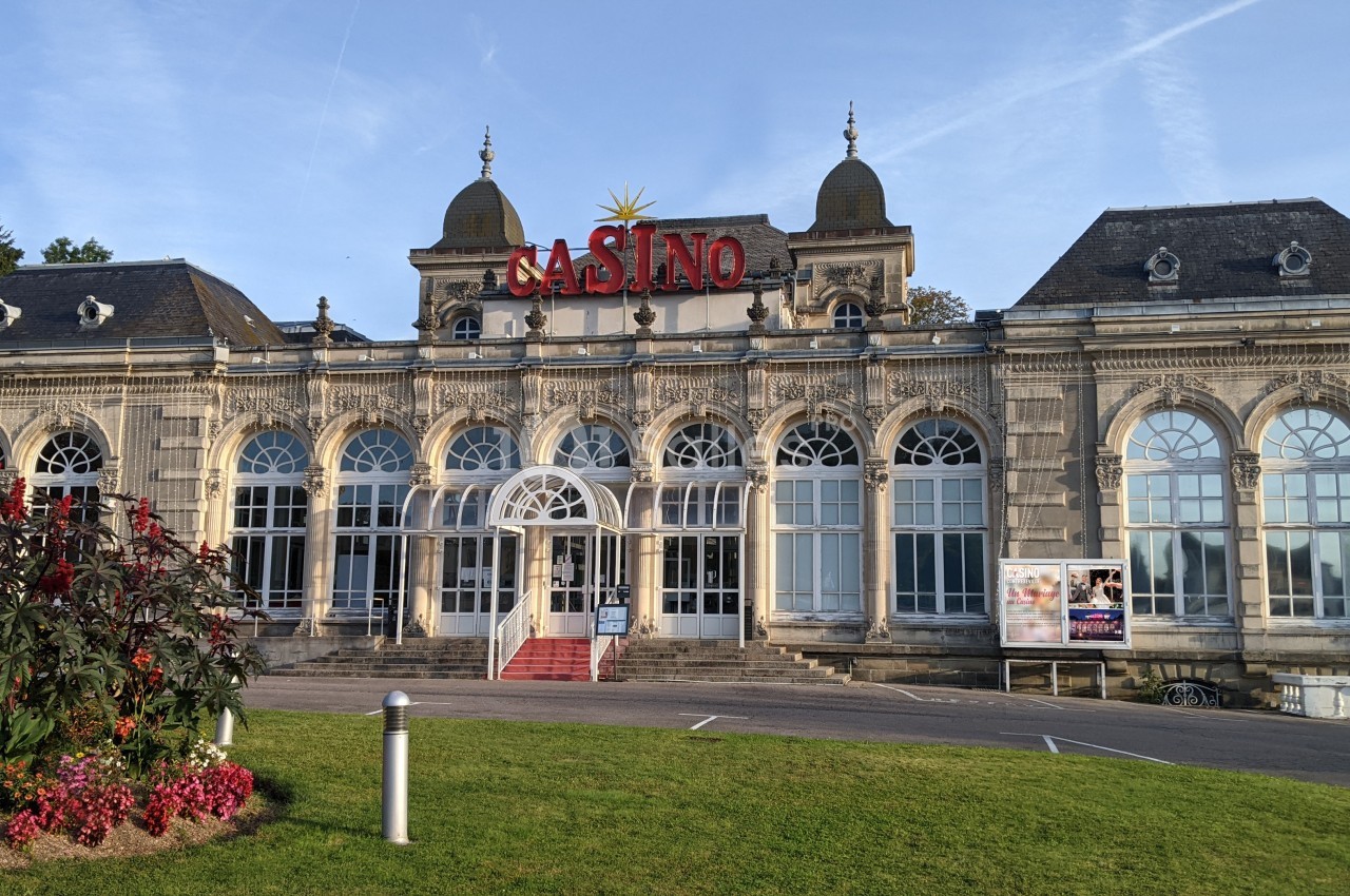 Façade d'un bâtiment historique abritant un casino, avec des jardins et une pelouse à l'avant.