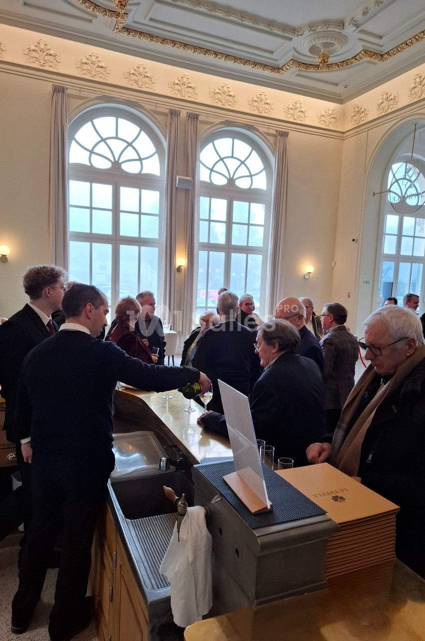 Un groupe de personnes échange dans une salle lumineuse avec de grandes fenêtres et un comptoir au premier plan.