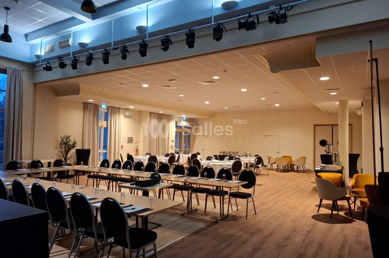 Salle de conférence lumineuse avec tables disposées en U, chaises alignées, et espace pour événements professionnels.