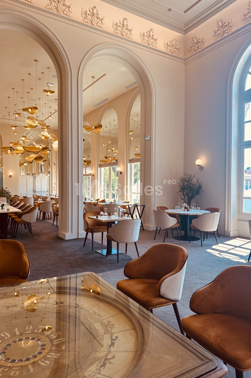 Salle de restaurant élégante avec de grandes arches, des lustres dorés et des fauteuils en velours marron.