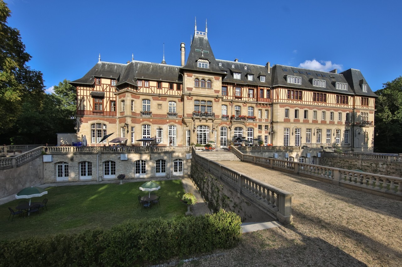 Façade d'un château de style classique avec colombages, entouré de jardins et d'une terrasse en pierre.