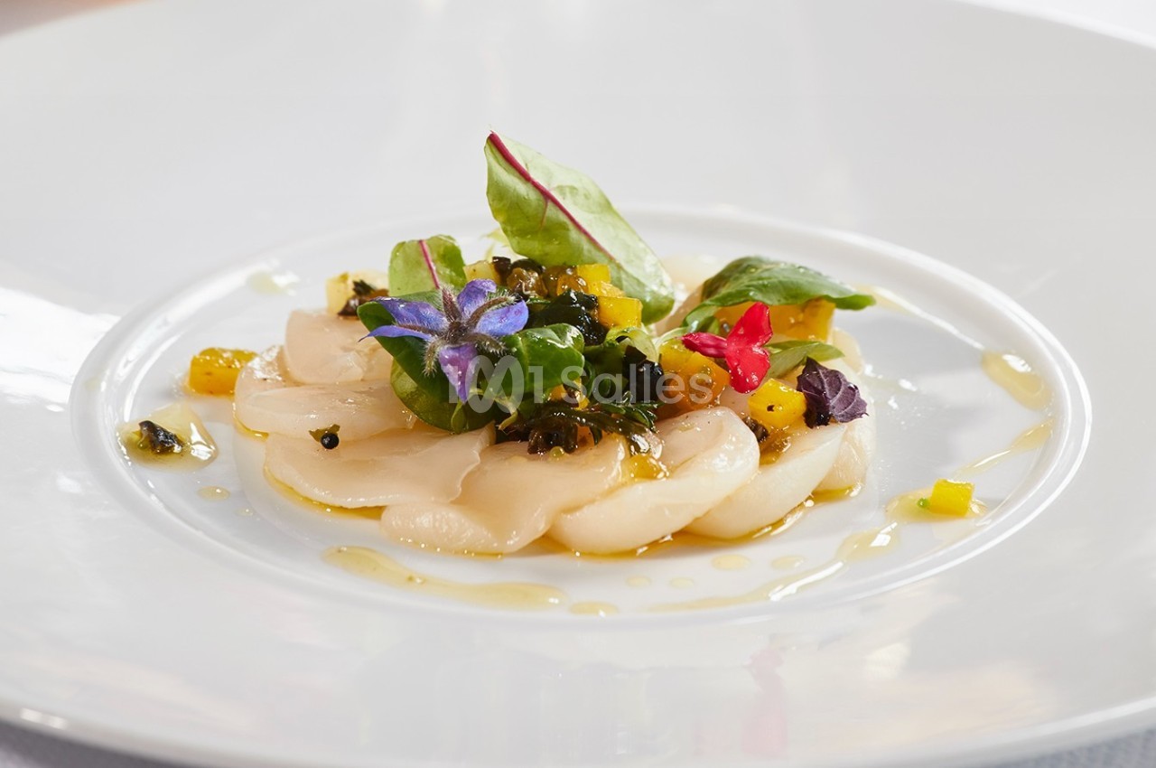 Tranches de coquilles Saint-Jacques crues garnies de fleurs comestibles, légumes colorés et feuilles vertes sur une assiette…