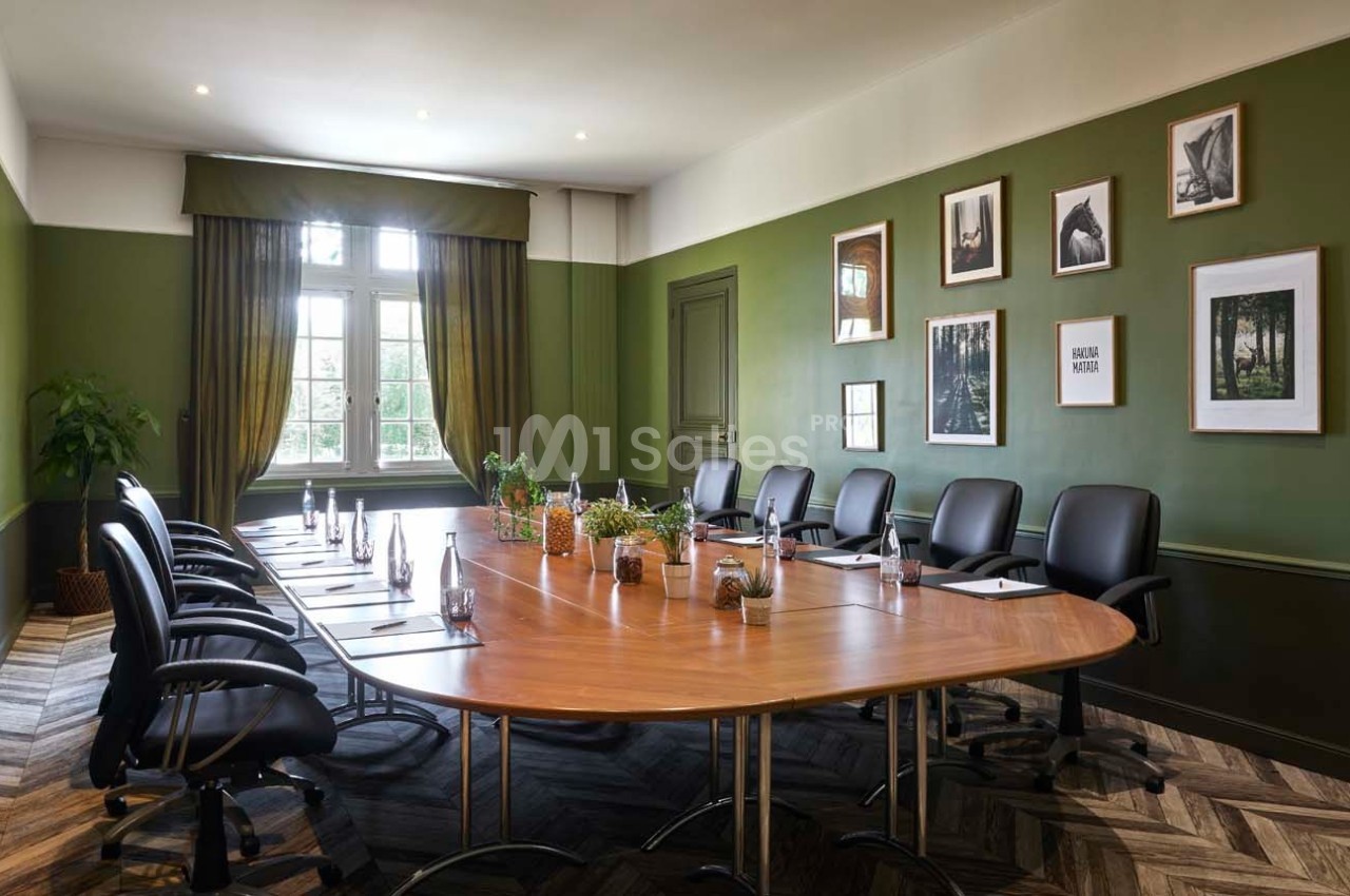 Salle de réunion lumineuse avec table ovale en bois, chaises noires, murs verts et décorations murales.