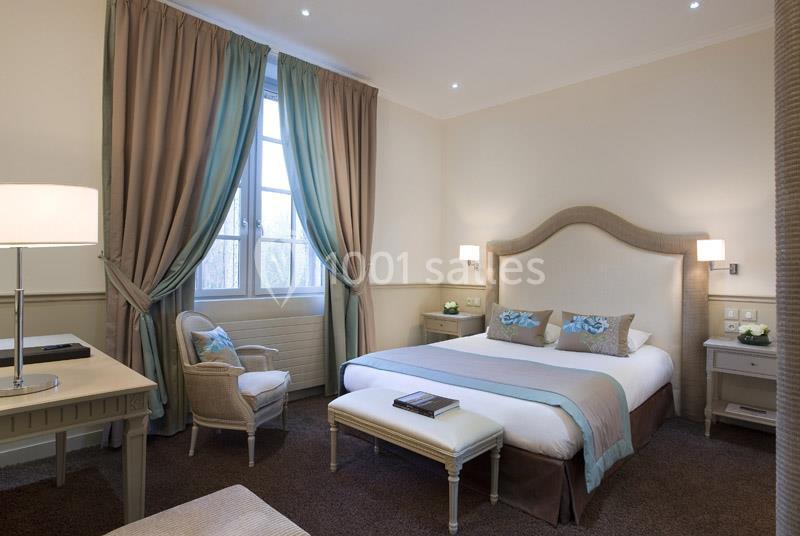 Chambre lumineuse avec un lit double, des rideaux beiges et verts, un bureau, une chaise et un éclairage doux.