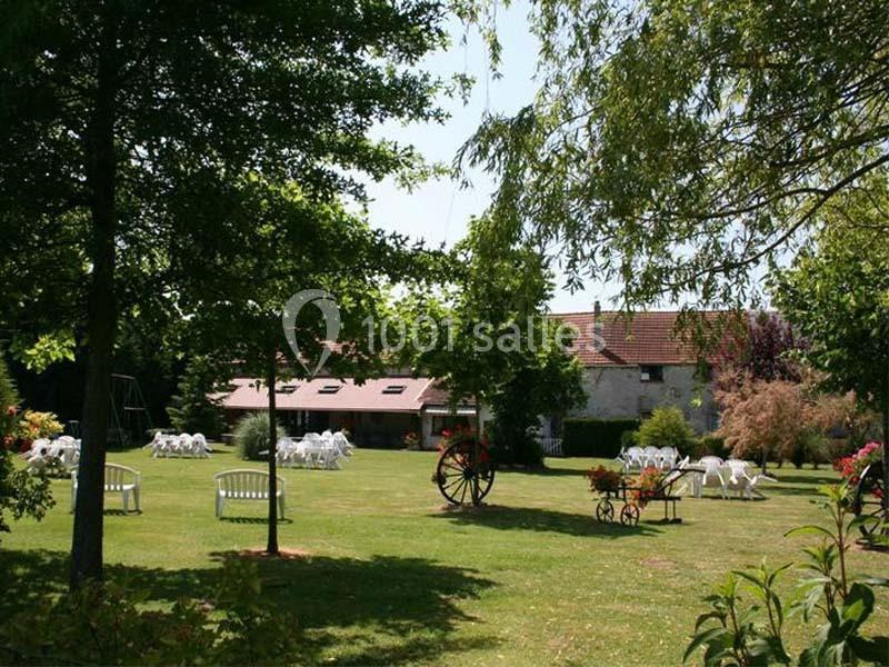 Jardin verdoyant avec des chaises blanches disposées sur la pelouse, entouré d'arbres et d'une maison en arrière-plan.