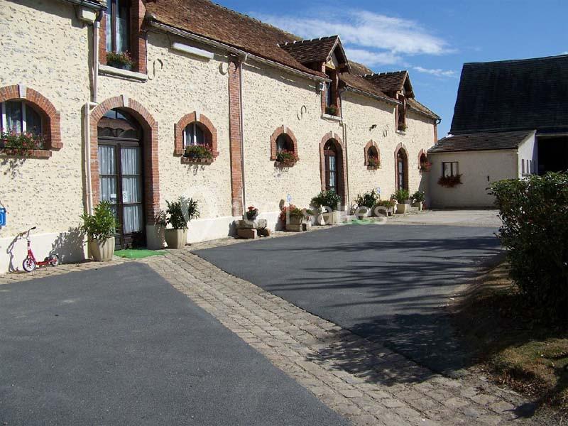 Façade d'un bâtiment en pierre avec fenêtres en arc, pots de fleurs et une allée pavée bordée de végétation.