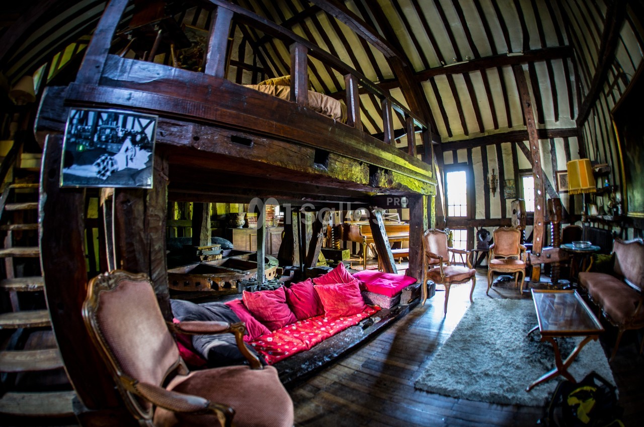 Salon rustique avec poutres apparentes, mezzanine en bois, canapé avec coussins colorés et meubles anciens.