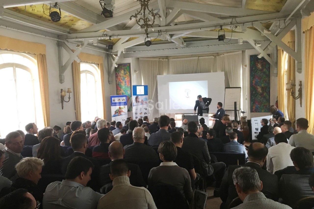 Salle de conférence remplie de participants assis, regardant une présentation projetée sur un écran.
