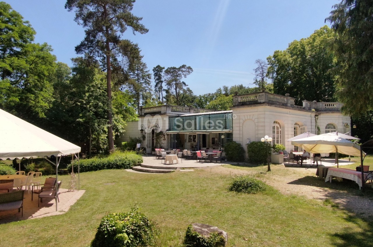 Bâtiment ancien entouré de verdure avec une terrasse aménagée et des tentes installées dans un jardin.