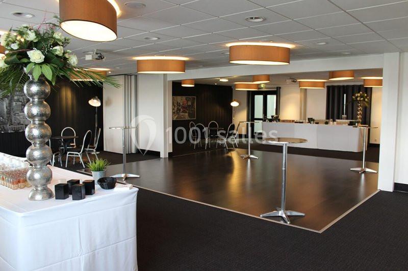 Salle de réception moderne avec tables hautes, chaises, éclairage suspendu et décoration florale.
