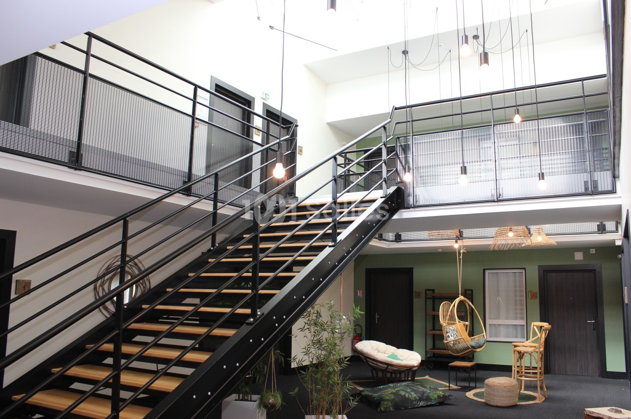 Escalier métallique moderne dans un espace intérieur lumineux avec mobilier en rotin et plantes décoratives.