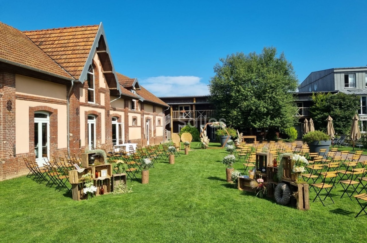 Jardin aménagé pour un événement avec chaises, décorations rustiques en bois et bâtiment en briques en arrière-plan.