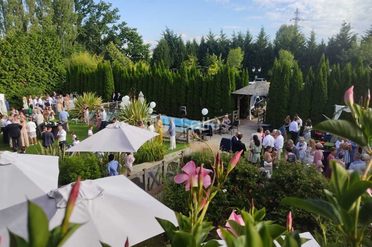 Groupe de personnes rassemblées dans un jardin avec piscine, entouré de végétation et de parasols.