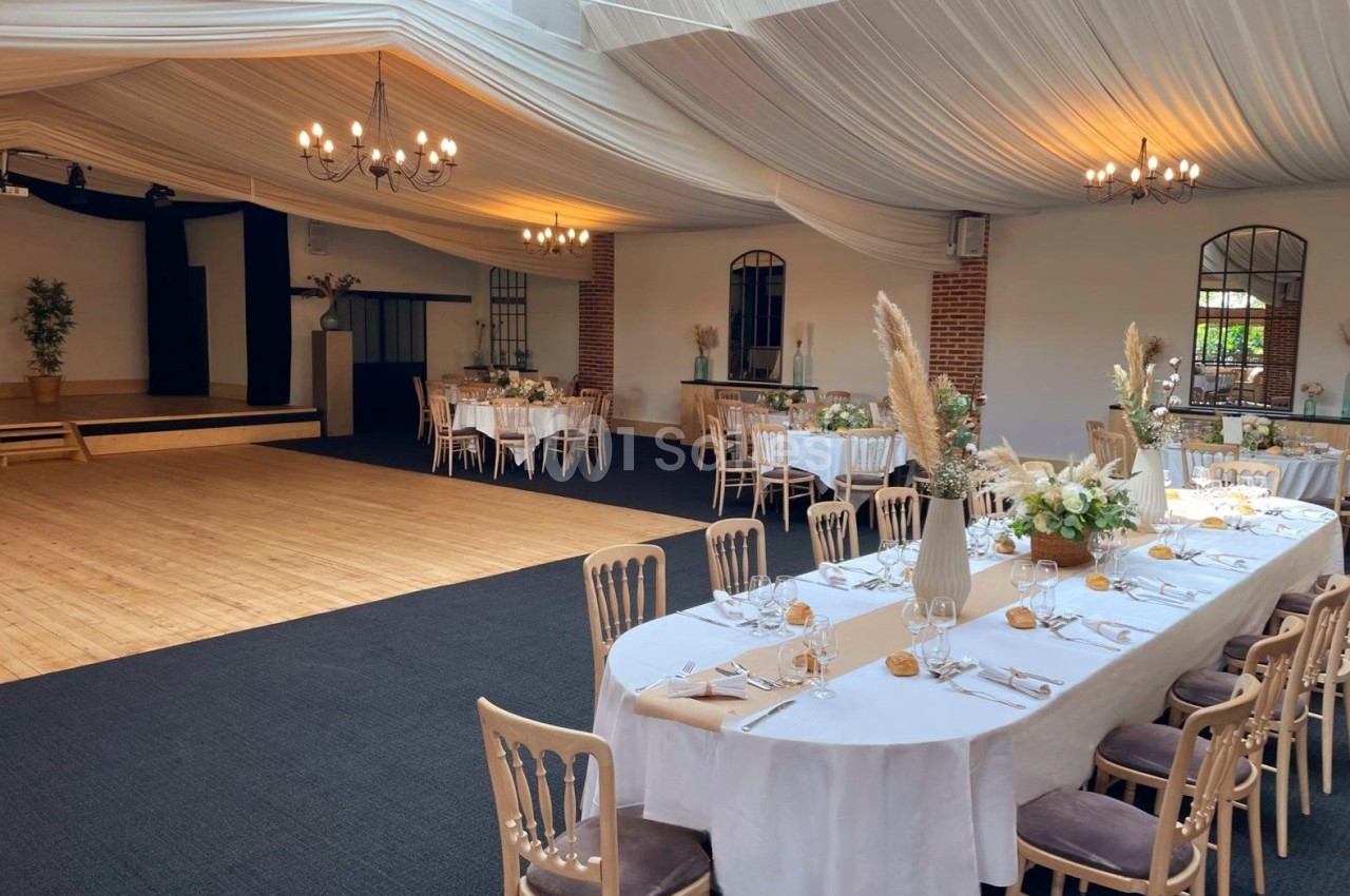 Salle de réception décorée avec des tables dressées, des chaises en bois clair et des arrangements floraux élégants.