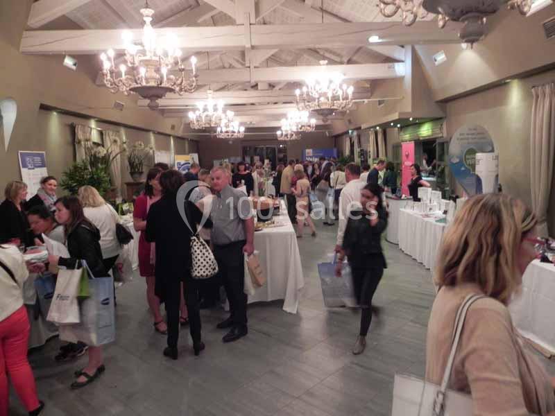 Des personnes discutent et explorent des stands dans une salle éclairée avec des lustres et des tables exposant des produits.