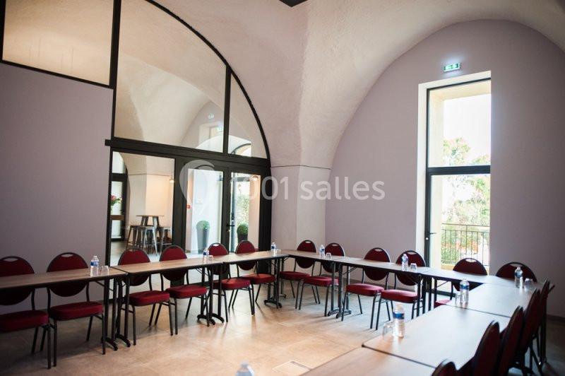 Salle de réunion lumineuse avec tables disposées en U, chaises rouges et grandes fenêtres laissant entrer la lumière…