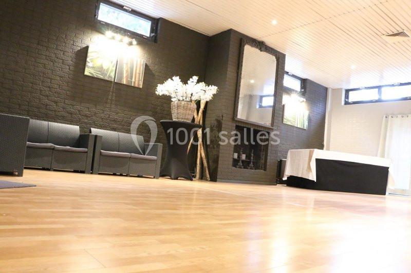 Salle lumineuse avec parquet, murs sombres, cheminée décorative, canapés, table drapée et vase de fleurs blanches.