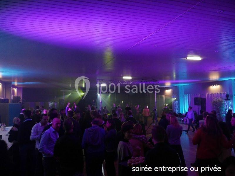 Salle éclairée par des lumières colorées, avec des groupes de personnes debout lors d'une soirée festive.