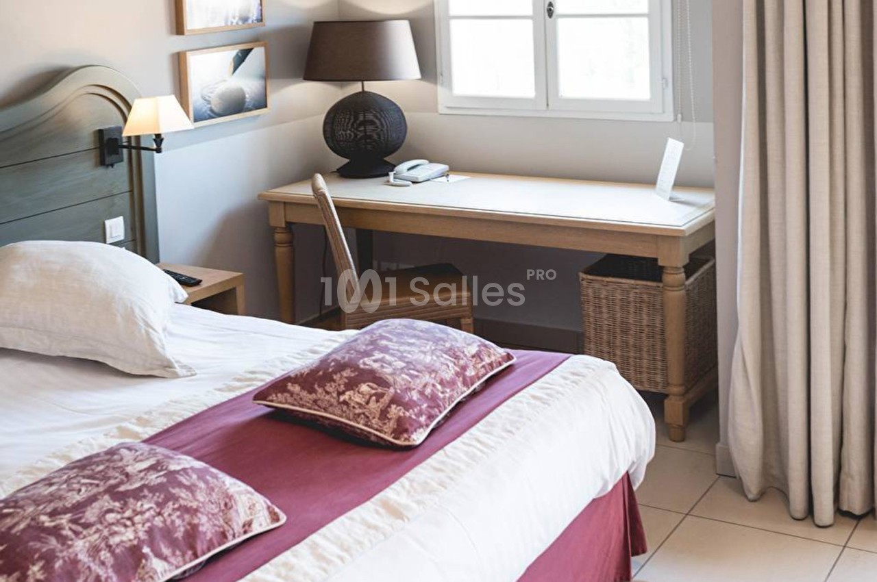 Chambre lumineuse avec lit double, bureau en bois près d'une fenêtre et décoration sobre.