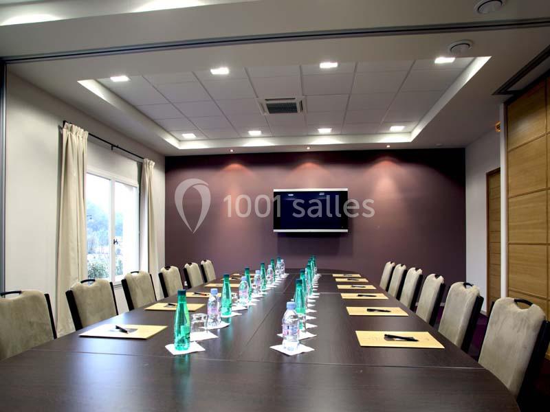 Salle de réunion avec une grande table rectangulaire, chaises alignées, bouteilles d'eau et écran mural.