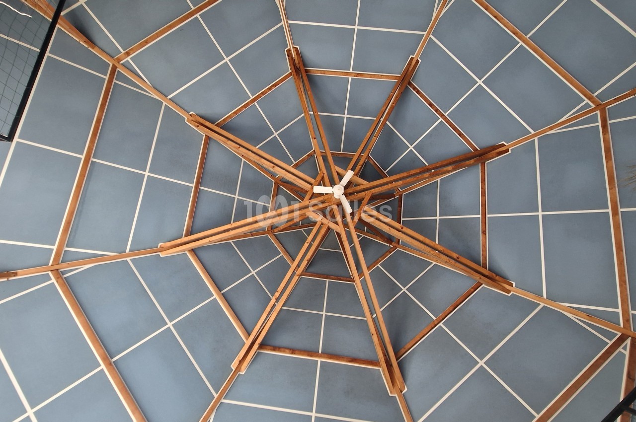 Structure en bois formant un motif géométrique complexe vue depuis le dessous, avec un plafond bleu quadrillé.