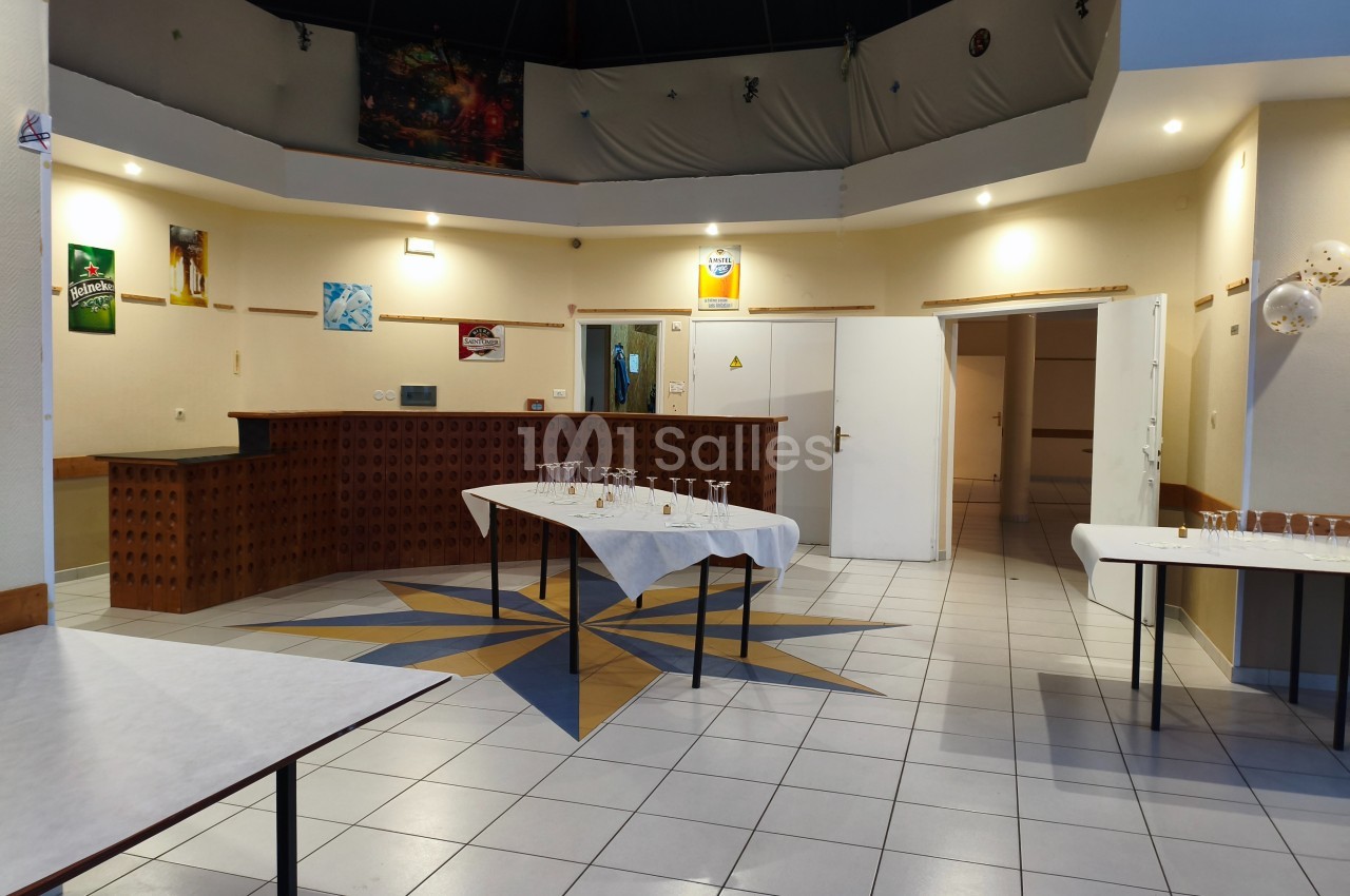 Salle de réception vide avec tables dressées pour un buffet, décor sobre et éclairage intérieur.