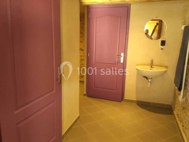 Salle de bain avec murs en pierre, porte violette, lavabo mural blanc et miroir rond.