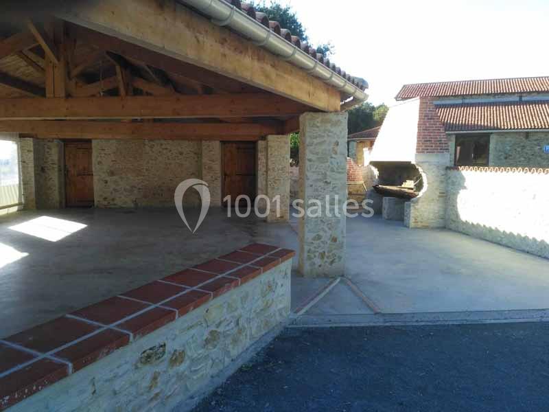 Abri en pierre avec charpente apparente, espace ouvert et barbecue intégré dans un mur extérieur.