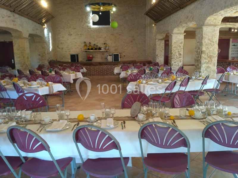 Salle de réception avec tables dressées, nappes blanches, chaises pliantes et décoration sobre en pierres apparentes.