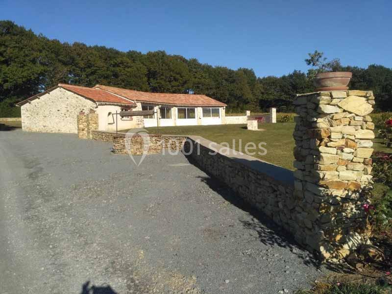 Maison en pierre avec toit en tuiles, entourée d'un jardin, d'un mur en pierre et d'une allée gravillonnée.