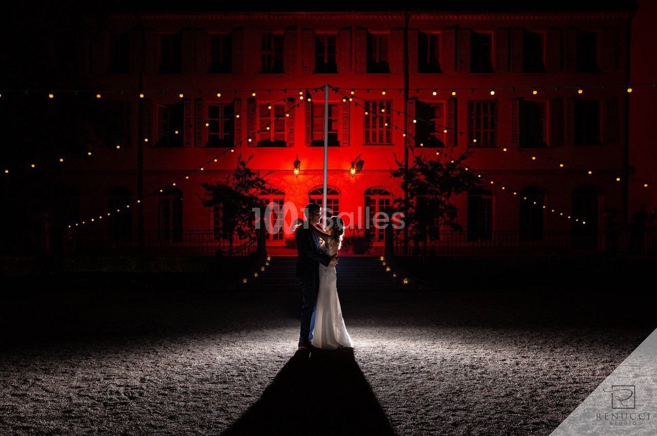 Un couple danse sous des guirlandes lumineuses devant un bâtiment éclairé en rouge, de nuit.