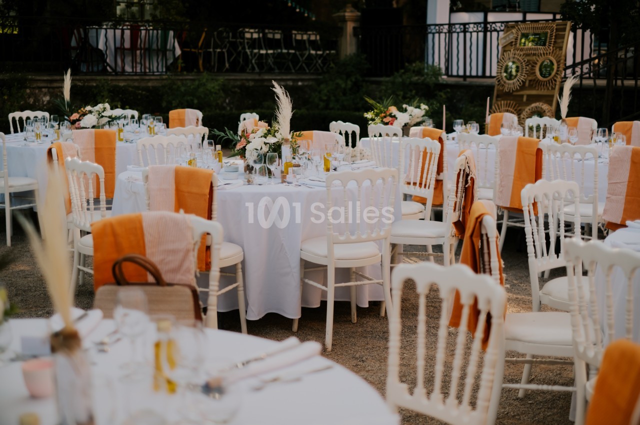 Tables rondes décorées de nappes blanches et chaises blanches avec des touches orange, disposées en extérieur.