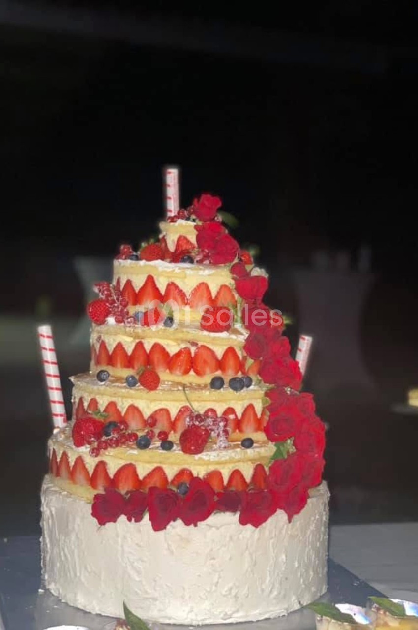 Gâteau à plusieurs étages décoré de fraises, myrtilles et roses rouges, avec des pailles en décoration.
