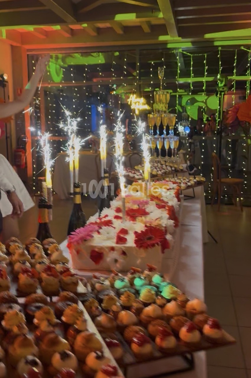 Table de desserts décorée avec des gâteaux, des fontaines lumineuses et une pyramide de coupes de champagne en arrière-plan.