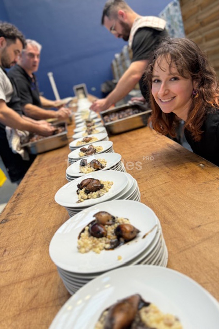 Des assiettes alignées contenant un plat à base de céréales et légumes, avec des cuisiniers en arrière-plan.