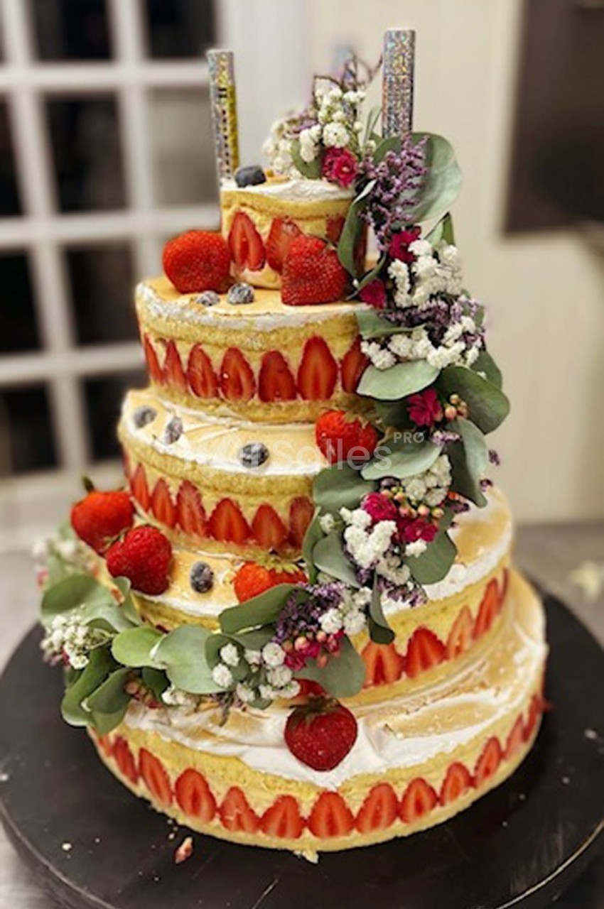 Gâteau de mariage à étages décoré de fraises, myrtilles, fleurs fraîches et bougies scintillantes.