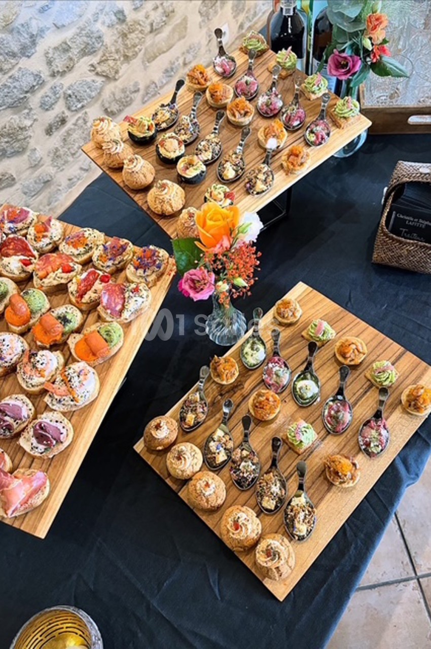 Plateaux en bois garnis de bouchées apéritives variées et colorées, disposés sur une table noire avec des décorations…