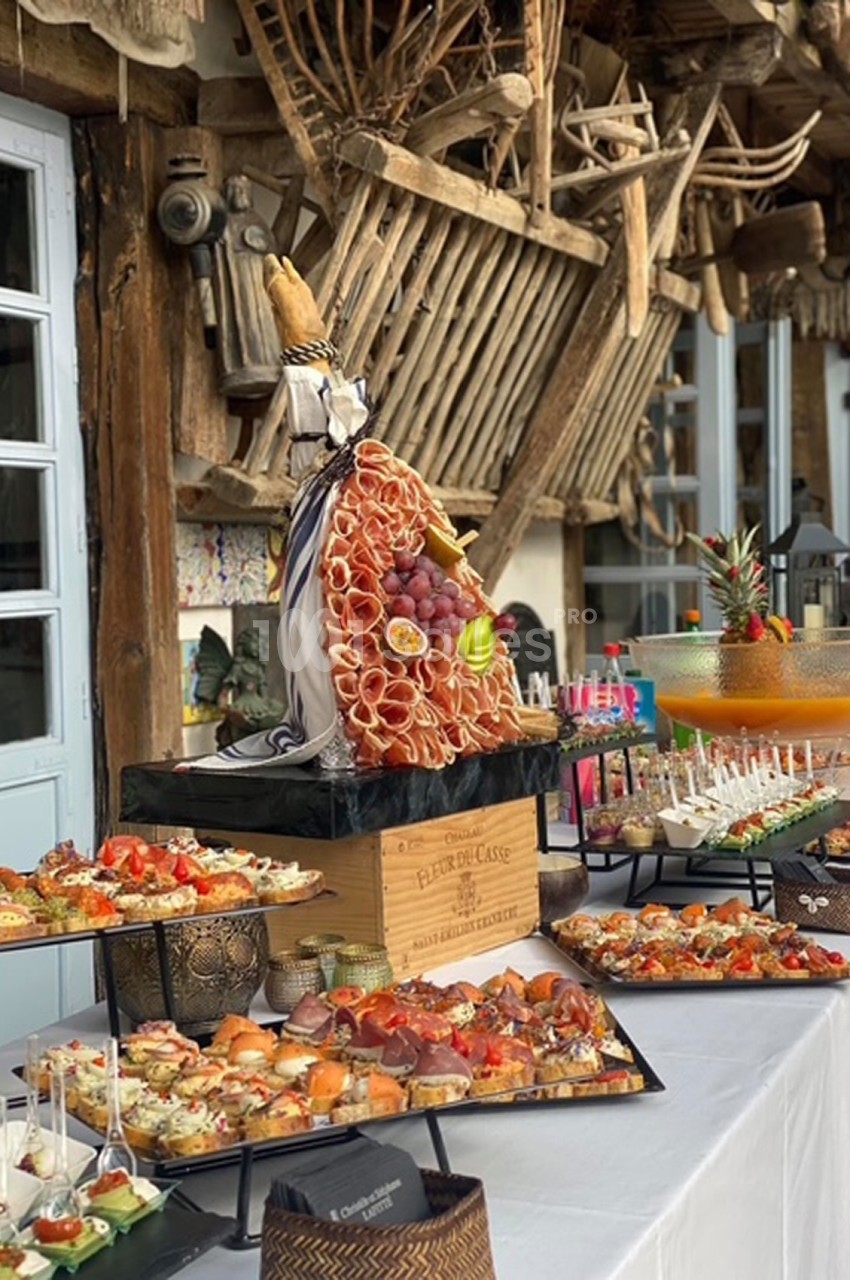 Plateau de charcuterie et fruits décoratif entouré de divers amuse-bouches sur une table lors d'un buffet en extérieur.