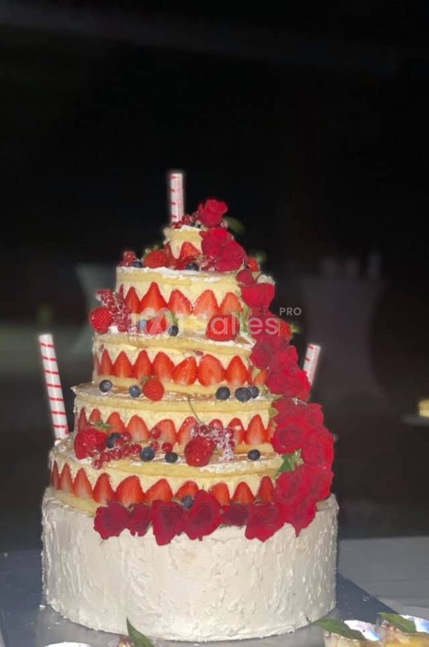 Gâteau à plusieurs étages décoré de fraises, myrtilles et roses rouges, avec des pailles en décoration.