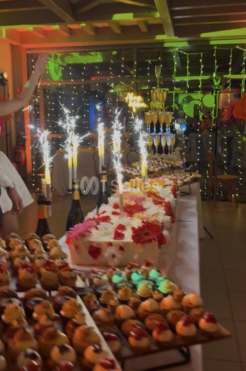 Table de desserts décorée avec des gâteaux, des fontaines lumineuses et une pyramide de coupes de champagne en arrière-plan.