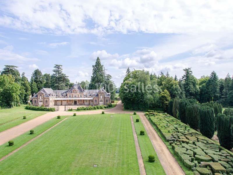 Vue aérienne d'un manoir entouré de jardins bien entretenus, avec des allées et des haies taillées.