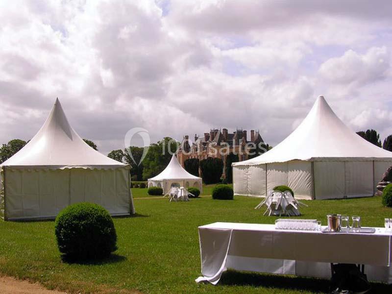 Tentes blanches installées sur une pelouse devant un château, avec des tables et des chaises disposées autour.