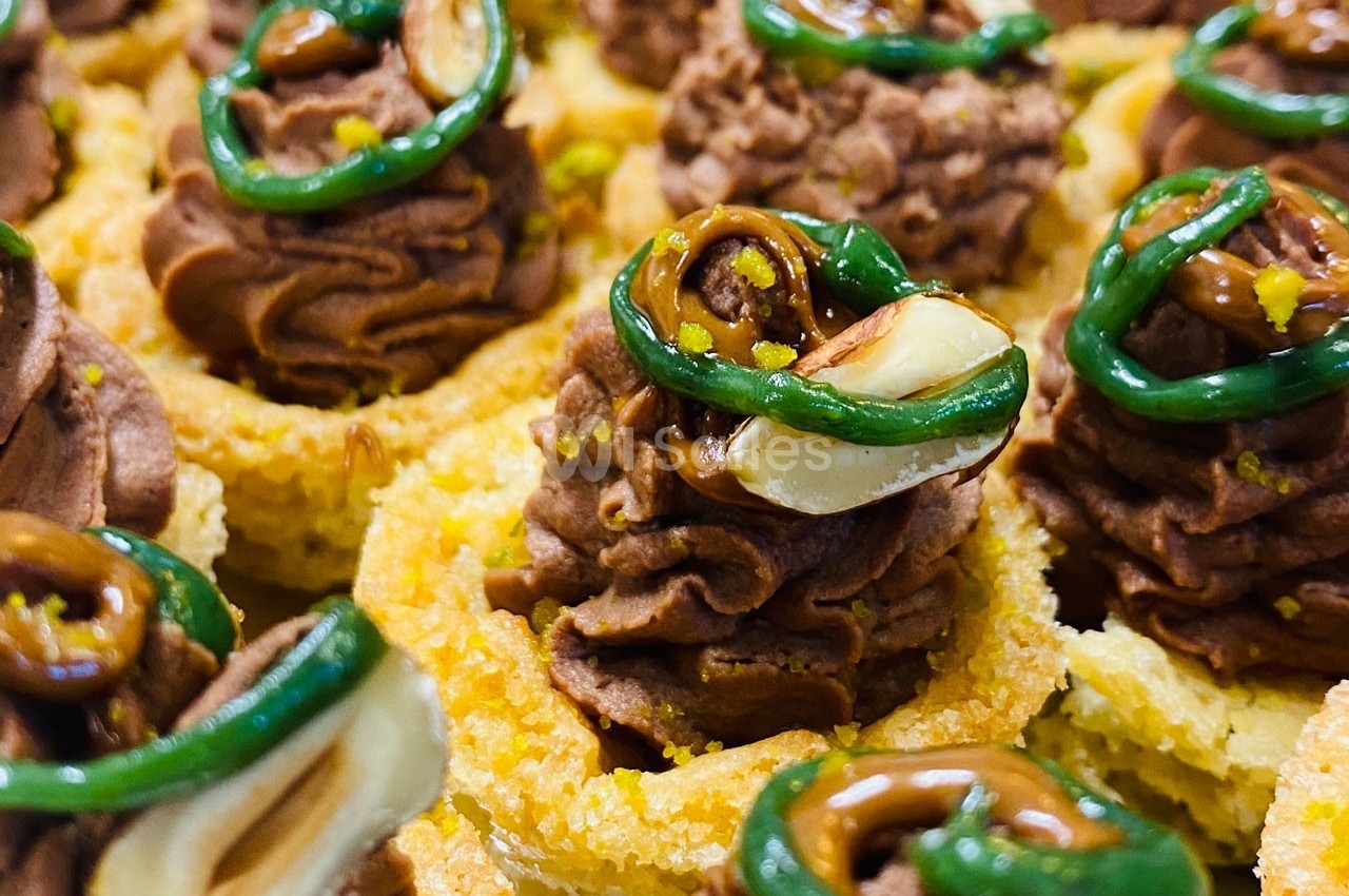 Tartelettes garnies de mousse au chocolat, décorées de noisettes, caramel et spirales de glaçage vert.
