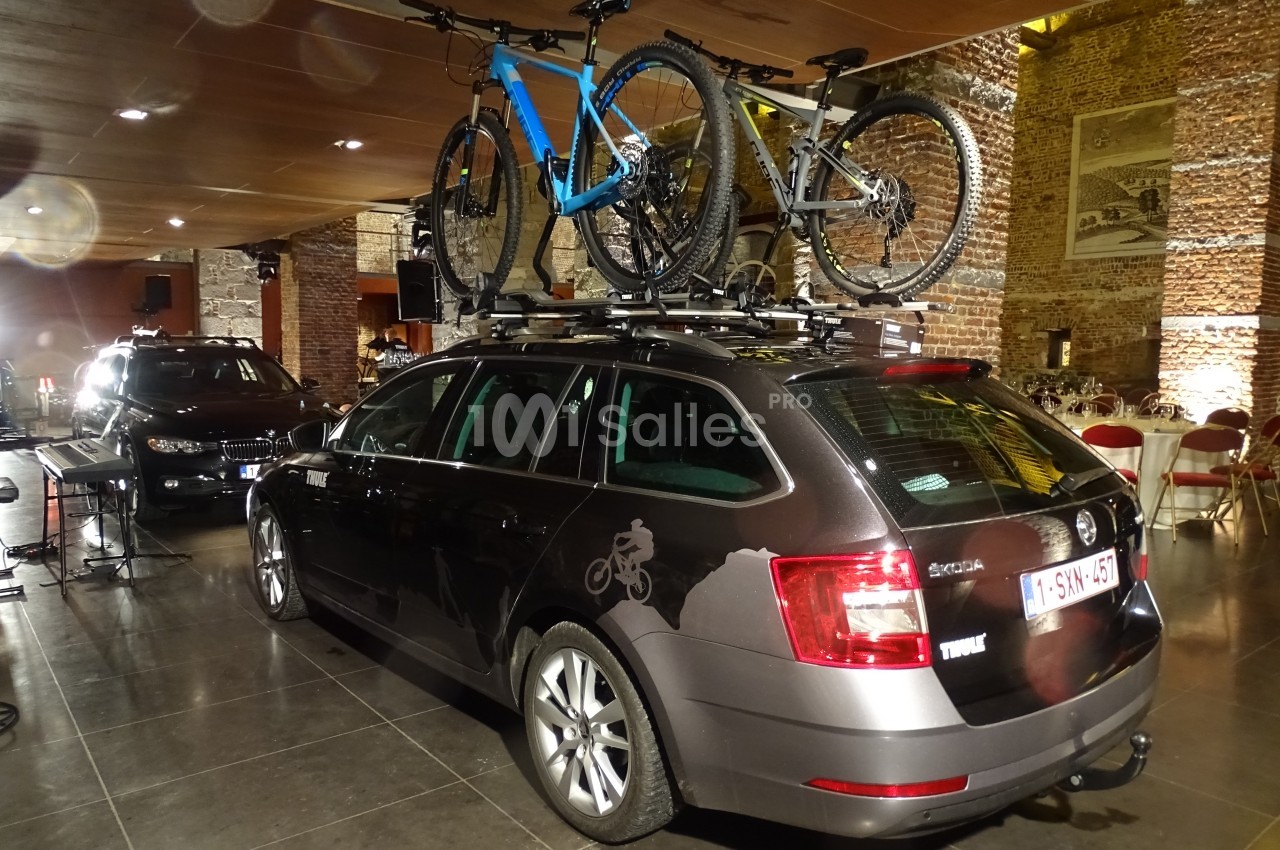 Voiture noire avec deux vélos fixés sur un porte-vélos de toit, stationnée dans un espace intérieur en briques.