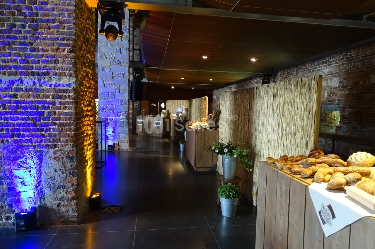 Salle avec murs en briques, éclairage tamisé, tables en bois garnies de pains et décorations végétales.